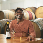 Banele Vakele, one of the contestants of the show, sitting down with a glass of wine and bottle in front