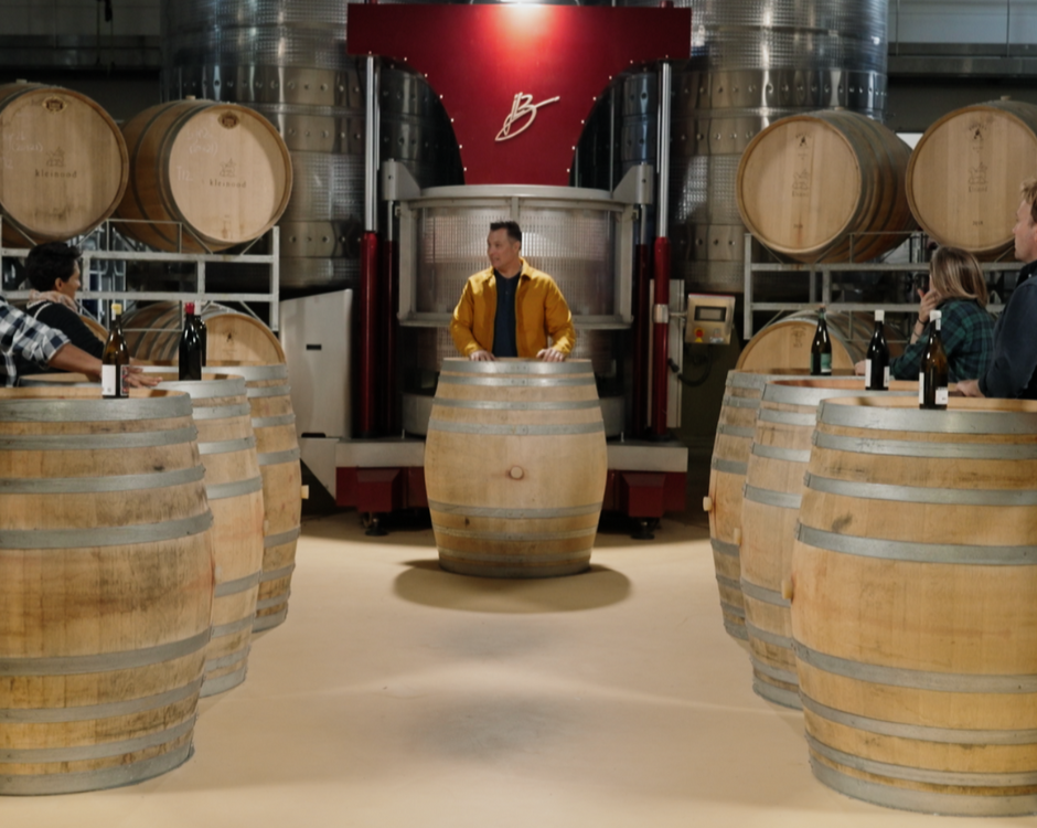 Episode 6 - Die Top 3 Word Aangekondig! illustrated by the contestants and host standing around wine barrels during the recording
